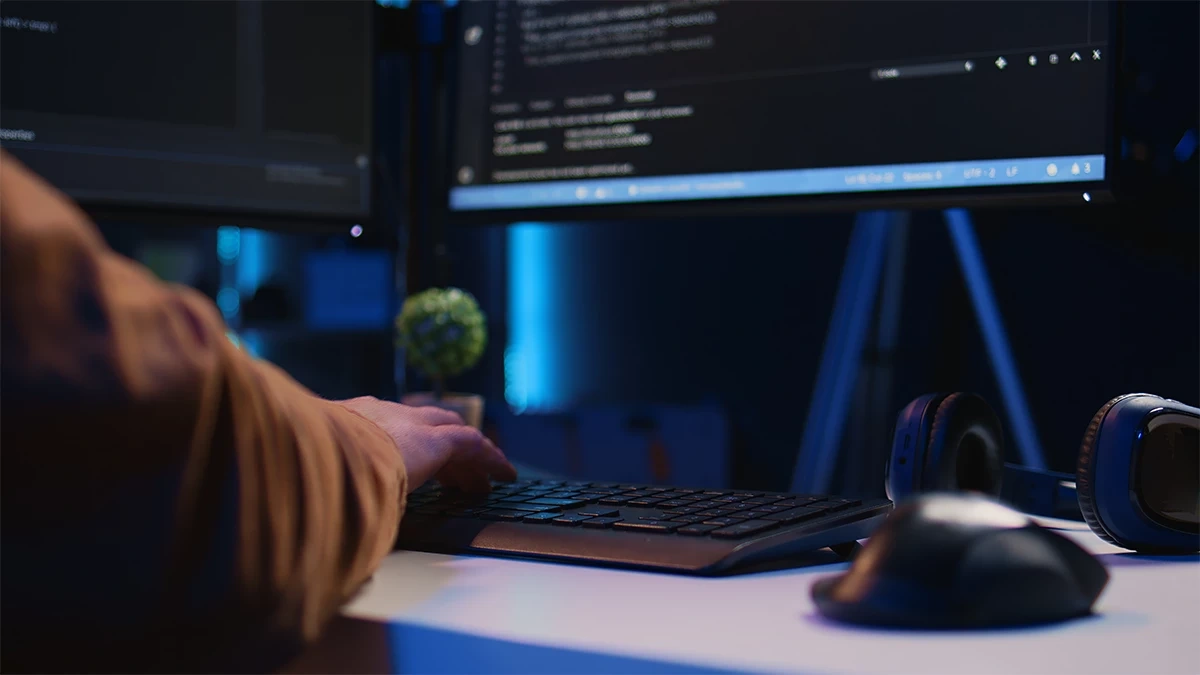 Close-up of developer’s hands coding Django applications on dual monitors in a dark office environment