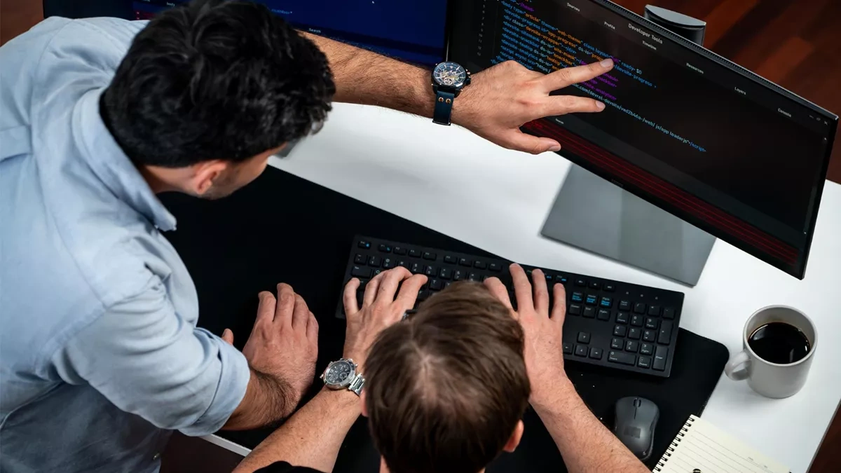 Two local web developers reviewing code on a desktop monitor, discussing a website project in a collaborative workspace.